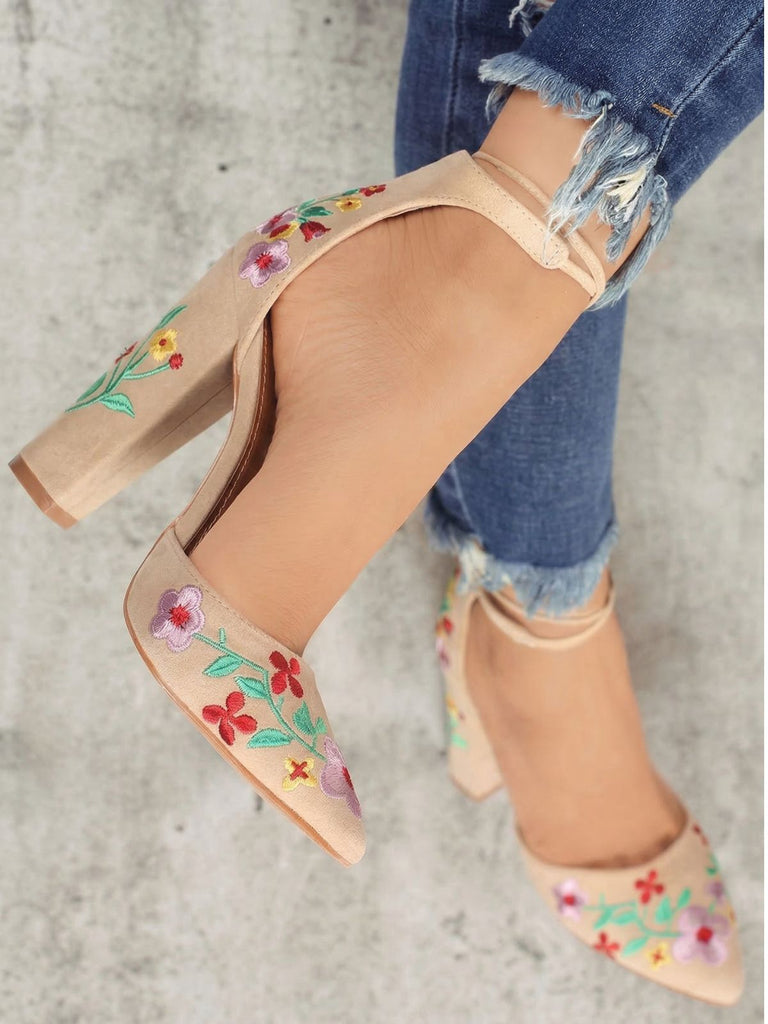 Beige High Heels mit Blumenstickerei, getragen zu zerrissenen Jeans vor einem neutralen Hintergrund