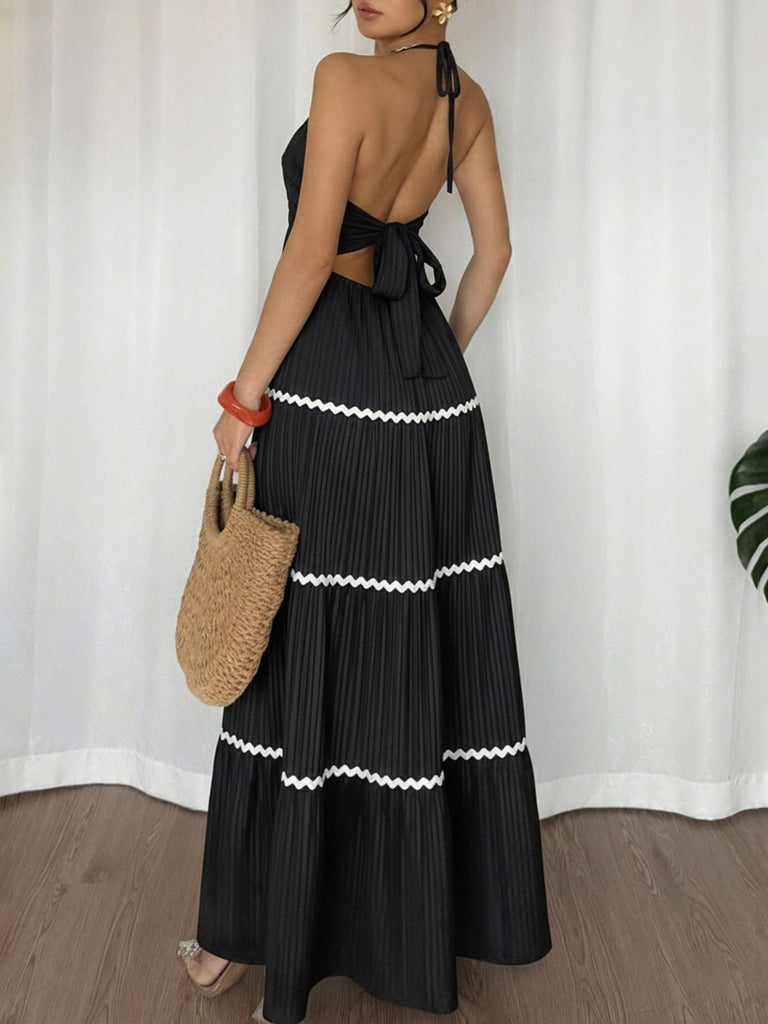 Frau in einem schwarzen Kleid mit weißem Besatz, die vor einem weißen Vorhang eine Strohtasche hält.