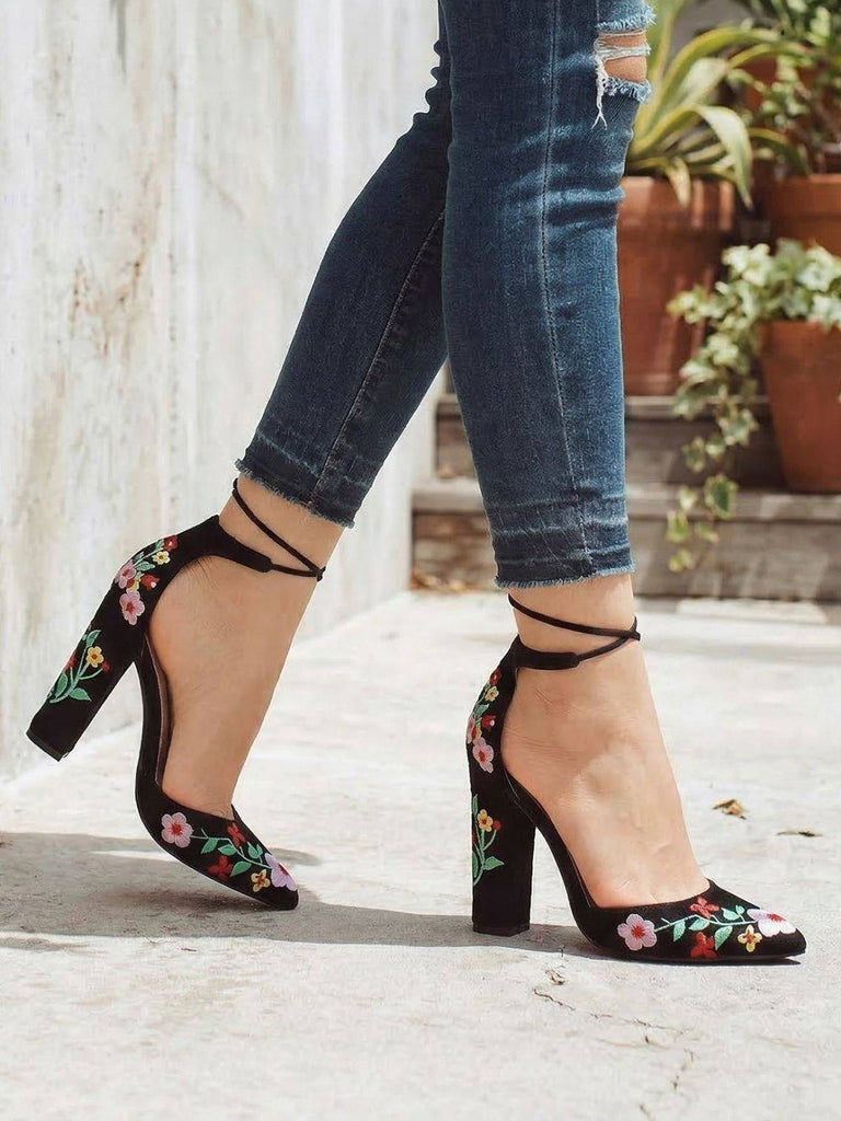 Schwarze Schuhe mit Blockabsatz und Blumenstickerei, getragen zu blauen Jeans vor hellem Hintergrund.