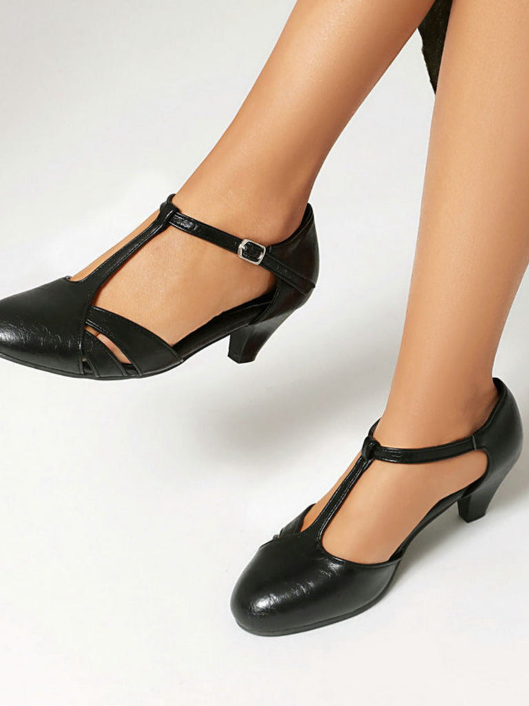 Schwarze Lederschuhe mit T-Riemen, getragen von einer Person vor weißem Hintergrund