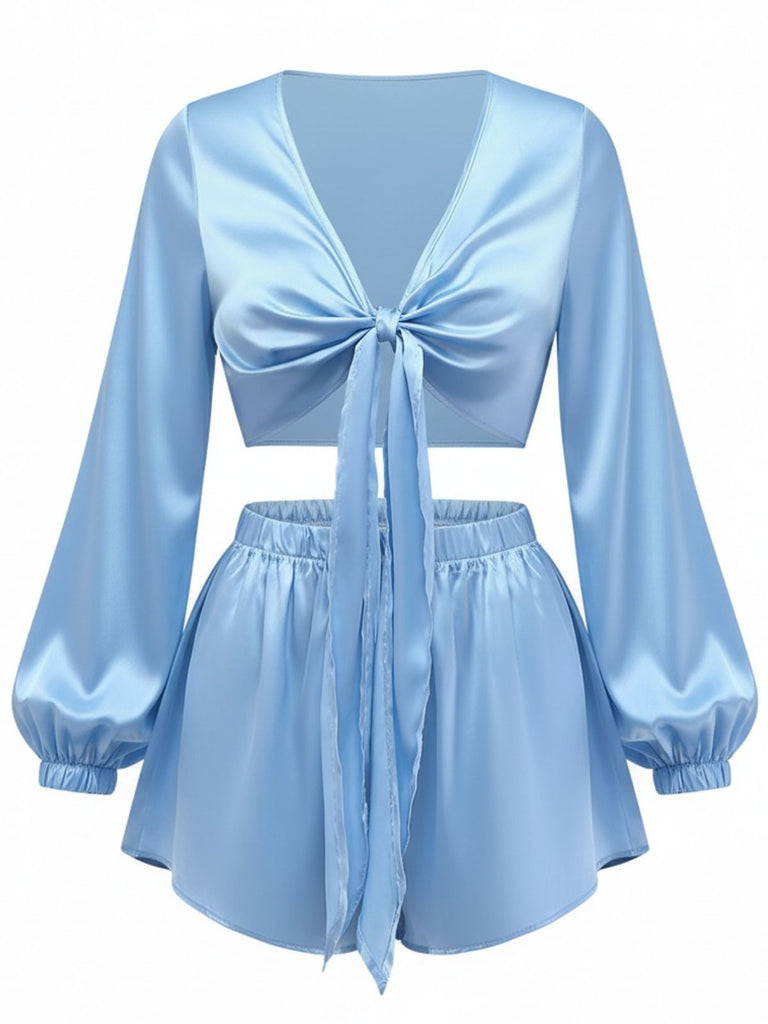 Ein hellblaues, zweiteiliges Loungewear-Set aus seidigem Satin, bestehend aus einem kurzen Oberteil mit Bindeband vorne und langen Ballonärmeln sowie passenden Shorts mit hohem Bund.