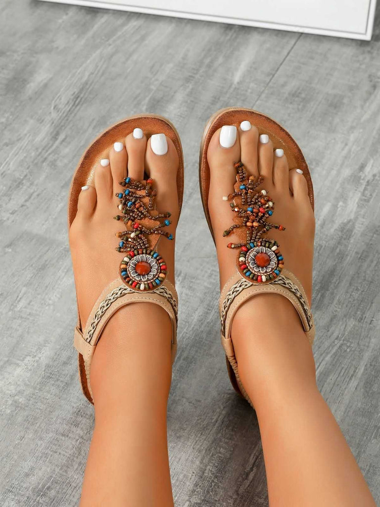 Beige Sandalen mit dekorativen Verzierungen auf einem grauen Holzboden.