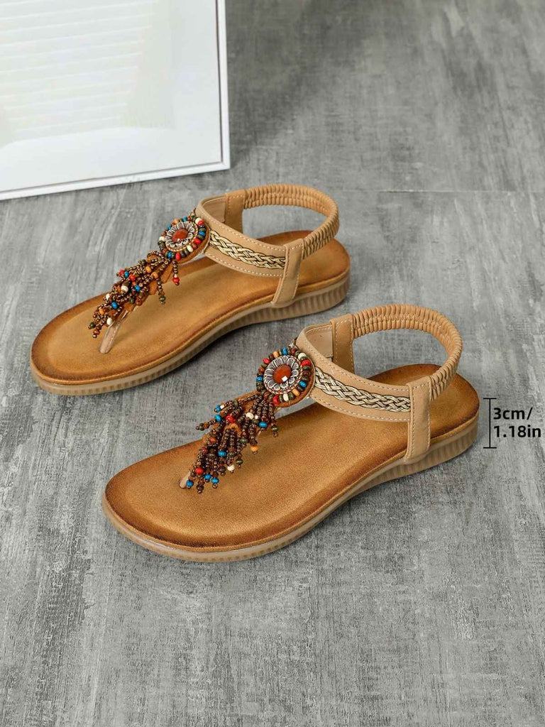 Paar hellbraune Sandalen mit Zierriemen auf grauem Untergrund