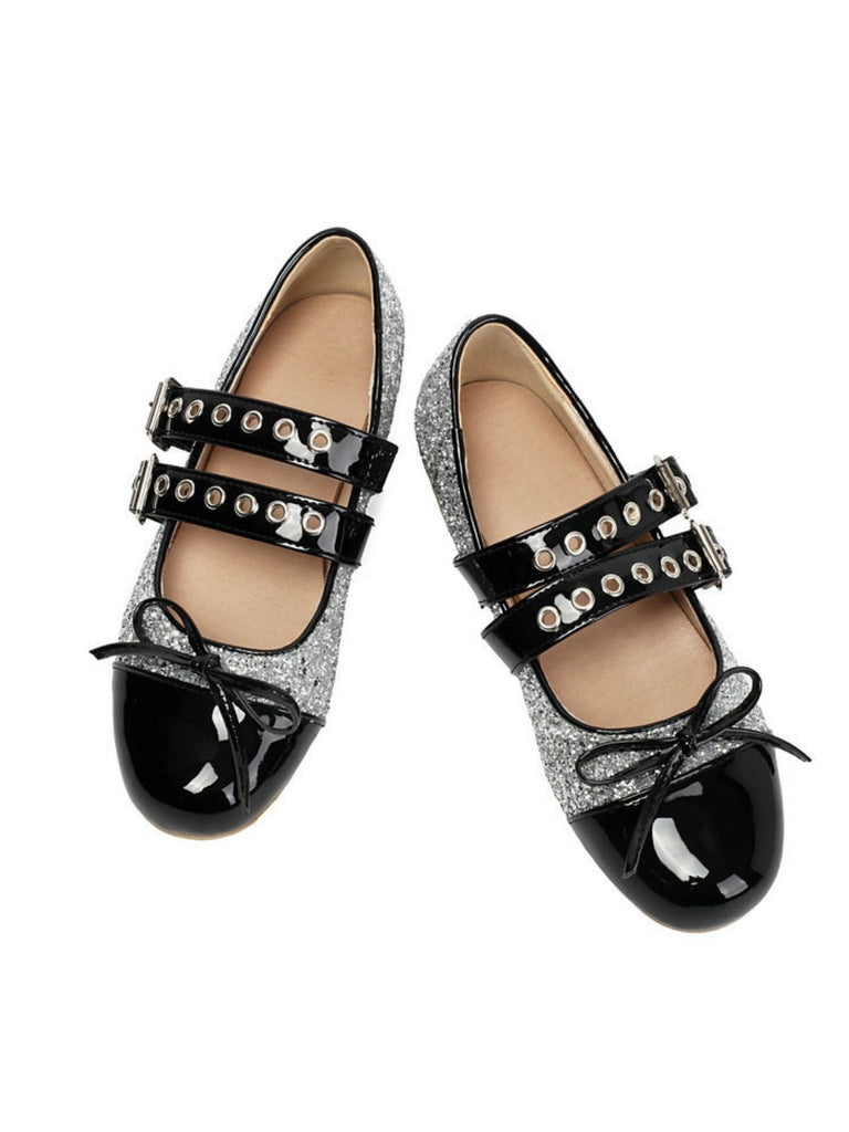 Ein Paar schwarze und silberne Glitzerschuhe mit Lacklederakzenten auf weißem Hintergrund