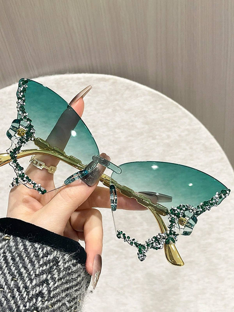 Sonnenbrille mit dekorativem gold-grünem Rahmen, in der Hand gehalten, vor neutralem Hintergrund