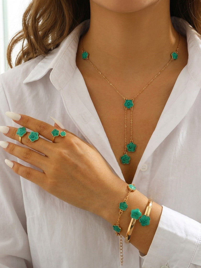 Frau mit grünem Schmuck, bestehend aus Halsketten, Ringen und Armbändern mit grünen Edelsteinen, auf einem weißen Hemd.