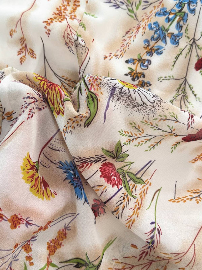 Nahaufnahme eines floralen Stoffes mit bunten Blumen und Blättern auf beigem Hintergrund