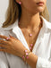 Person, die vor weißem Hintergrund eine rosa Halskette mit rosa Blumenanhängern, einen passenden Ring und ein Armband trägt.