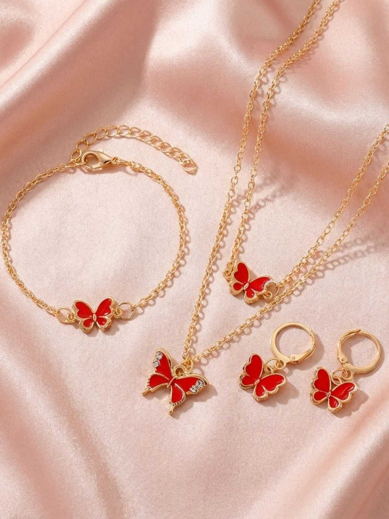 Goldfarbenes Schmuckset mit roten Schmetterlingsanhängern auf rosa Stoffhintergrund