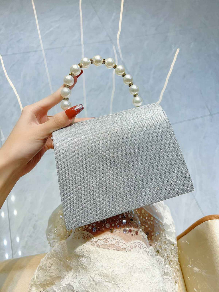 Silberne Clutch mit Perlmuttgriff, von einer Hand gehalten, vor hellblauem Hintergrund