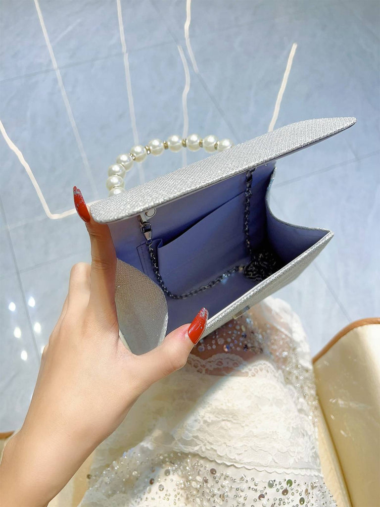 Hand hält eine silberne Clutch mit Perlmuttgriff vor hellblauem Hintergrund