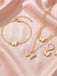 Goldschmuckset mit Schmetterlingsanhängern auf rosa Stoffhintergrund