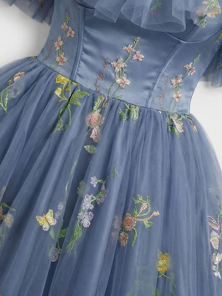 Nahaufnahme des Kleidoberteils, die die aufwendige Blumen- und Schmetterlingsstickerei auf einem strukturierten, staubblauen Netzstoff zeigt.