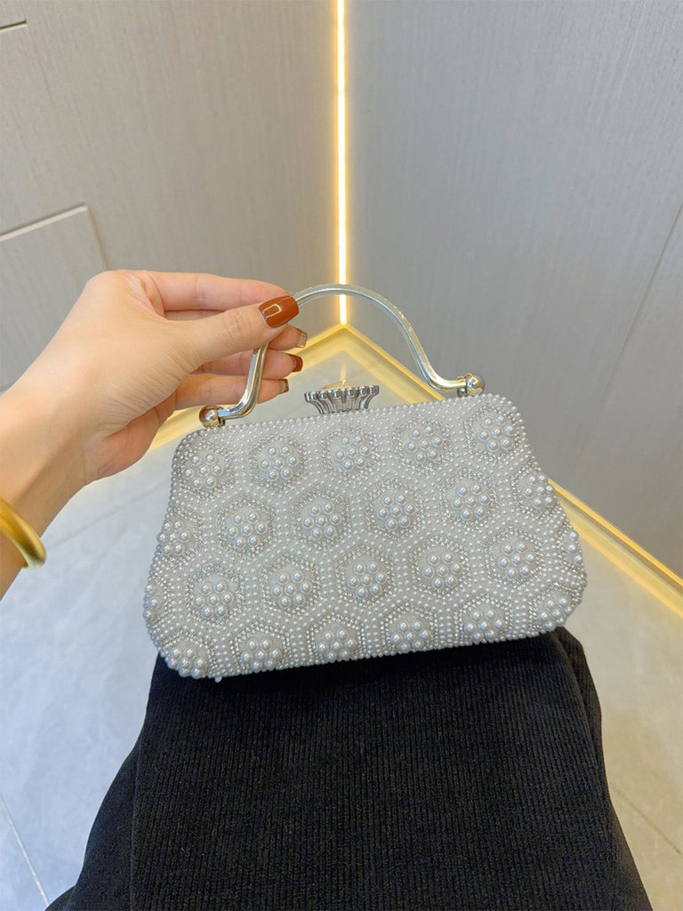 Hand hält eine Perlenhandtasche vor neutralem Hintergrund